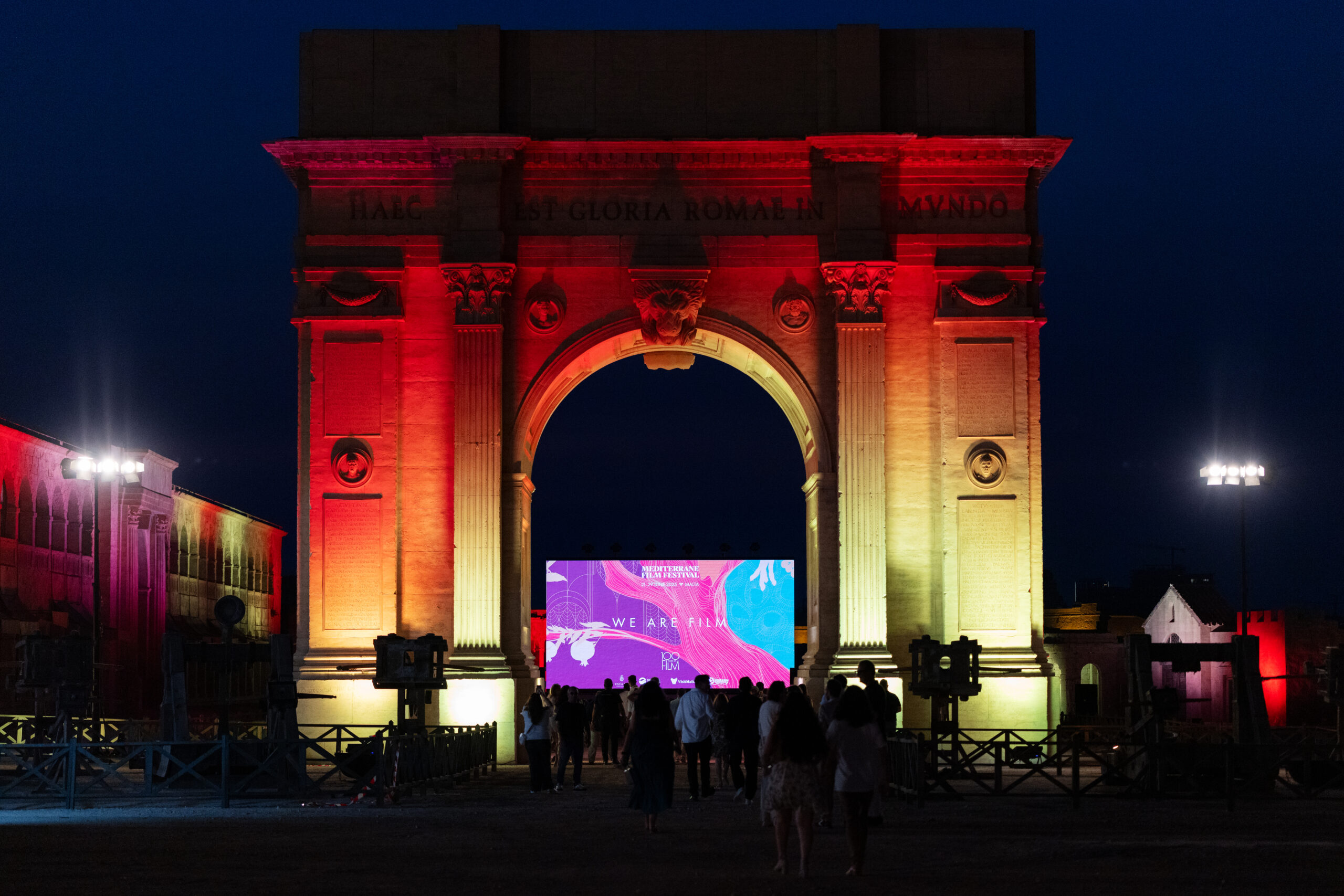 A red-and-yellow lit up archway houses a film screen under the arch and a crowd of people stands in front of the arch during MFF’s opening ceremony