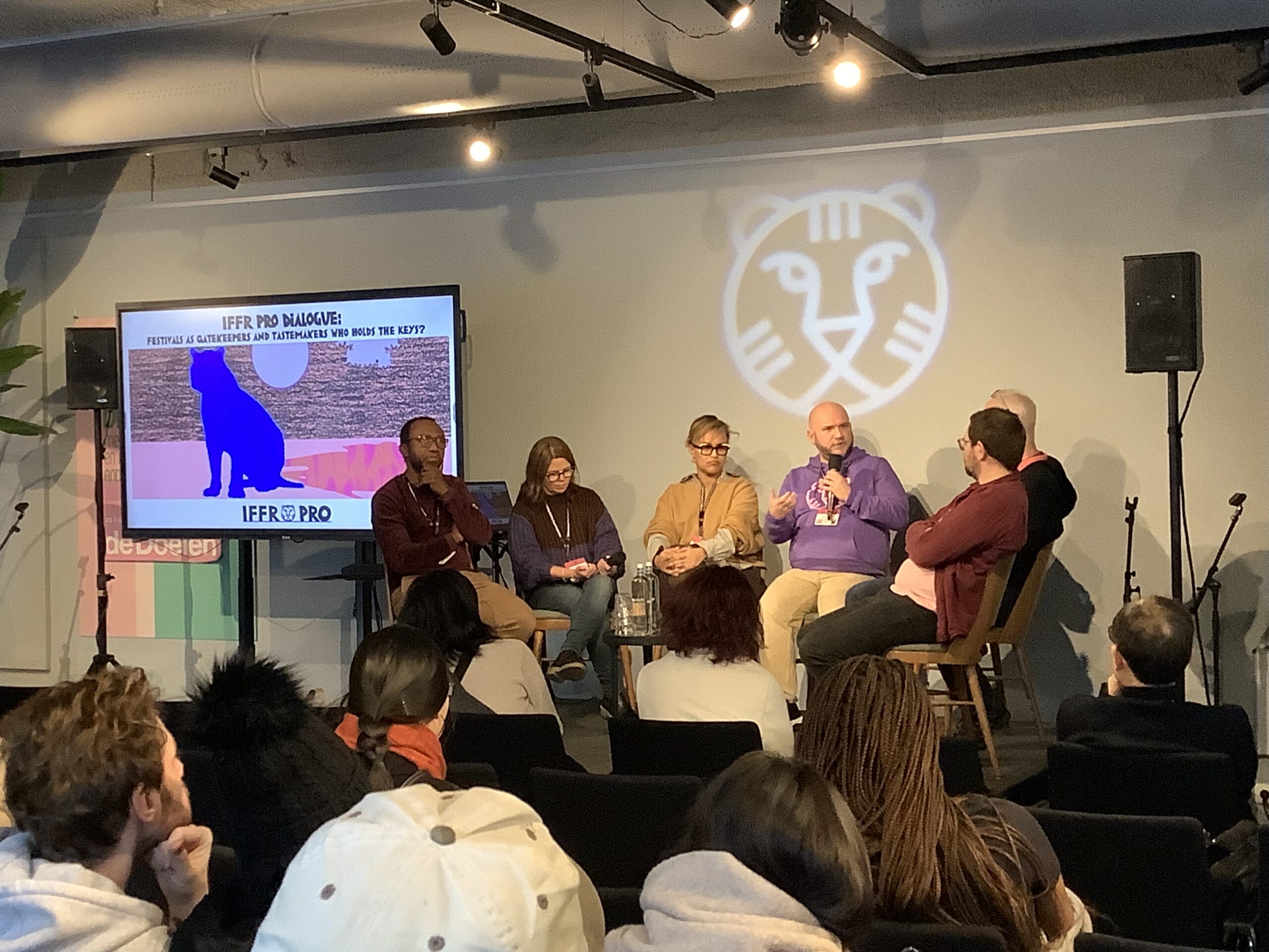 A panel of experts sits in front of an audience at IFFR Pro, with a TV screen to the left.